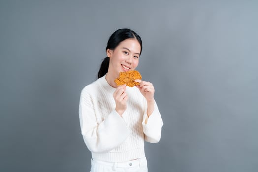 Young Asian woman wearing a sweater with a happy face and enjoy eating fried chicken on grey background photo