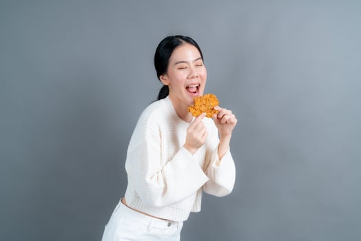 Young Asian woman wearing a sweater with a happy face and enjoy eating fried chicken on grey background photo