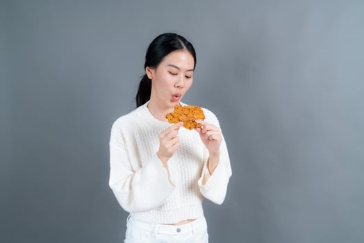 Young Asian woman wearing a sweater with a happy face and enjoy eating fried chicken on grey background photo