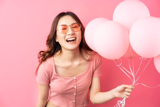 The beautiful lady wears glasses and holds balloons on a pink background photo