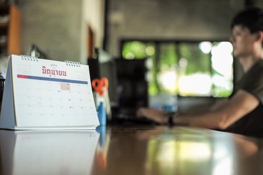 Closeup calendar on the table with blurred workman typing the keyboard of computer in background. Workfrom home concept. Thai word on the calendar mean June in English photo