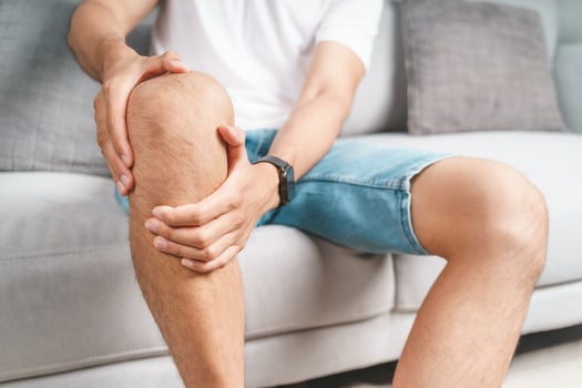 The man suffering from knee pain sitting on the couch hold and massaging his painful knee. photo