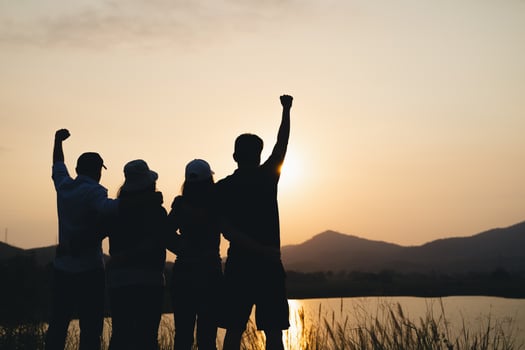 group of people with raised arms looking at sunrise on the mountain background. Happiness, success, friendship and community concepts. photo