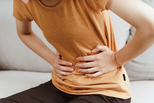 Young woman suffering from strong abdominal pain sitting on the couch at home. Gastritis, Period, menstruation. photo