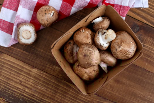 Baby bella mushrooms inside paper container on wooden table with cotton napkin photo