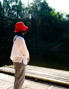 Rear view of lonely woman in red had sitting on the bamboo floor looking at the green forest and river photo