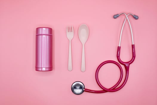 A pink stethoscope, spoon, fork, and thermos bottle on the pink background, flat layout photo