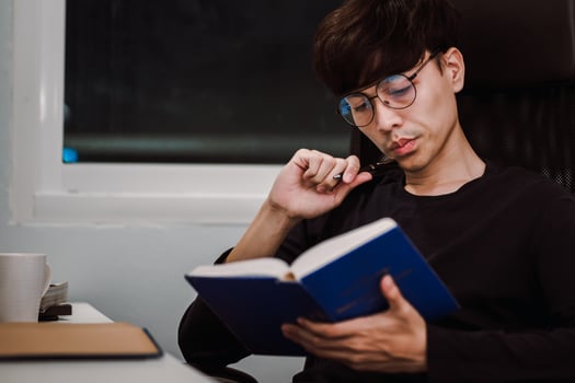 Young handsome asian man reading book at work desk late at night photo