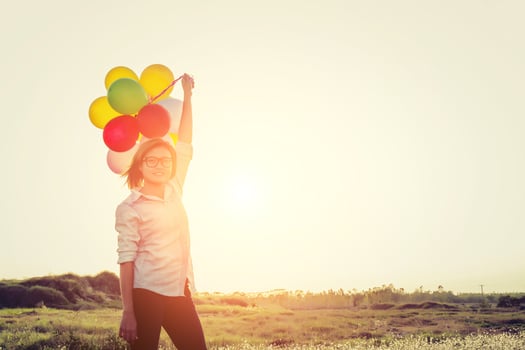 woman wearing glasses holding balloons in the field smiley to camera photo