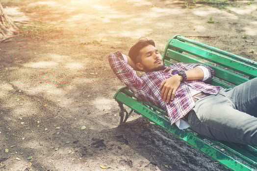 Young hipster man lying down on green park bench, looking away. photo