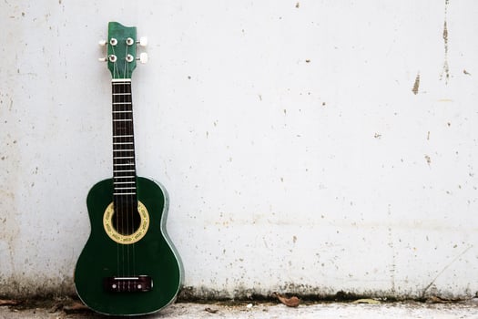 A green ukulele leaning against white wall photo