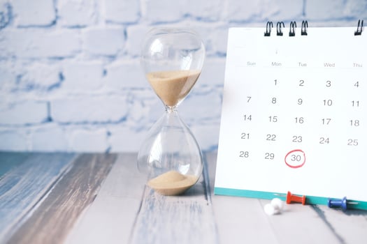 hourglass flowing through the bulb of sandglass and calendar on table photo