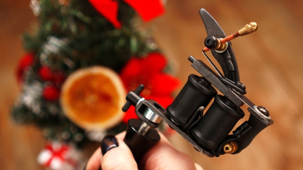 Female hand holding tattoo machine on blurred christmas tree photo