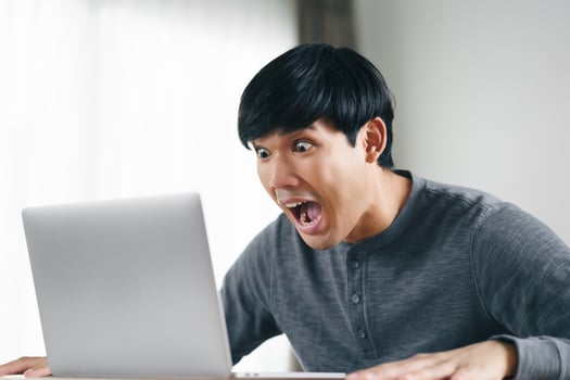 Surprised Asian man looking at laptop computer screen in living room. photo