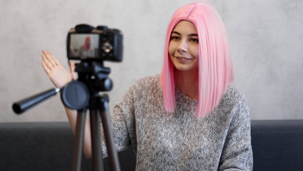 Happy girl blogger in pink wig in front of the camera on a tripod photo