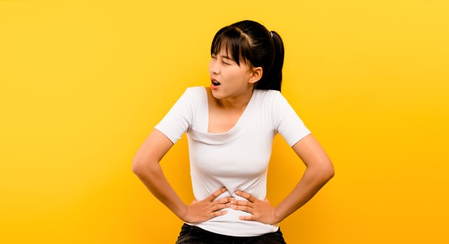 Asian woman with severe stomach ache alone on a yellow photo