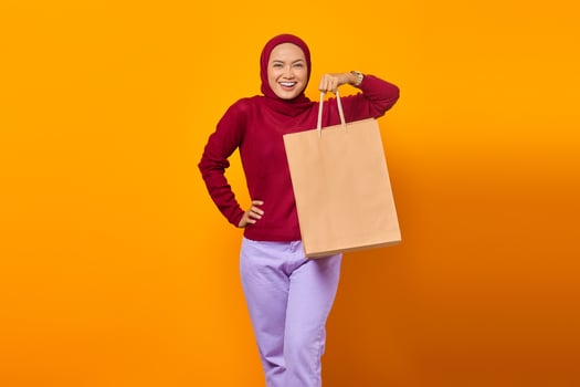 Cheerful Asian woman holding shopping bags over yellow background photo