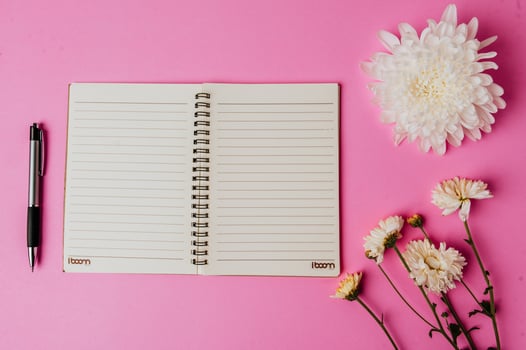 notebook, pen, blank card and flower on pink background photo