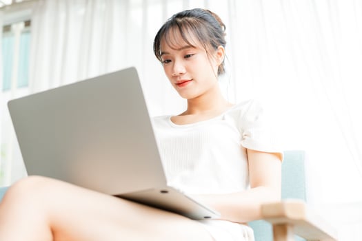 Portrait of young girl sitting on sofa at home using laptop and holding atm card in her hand photo