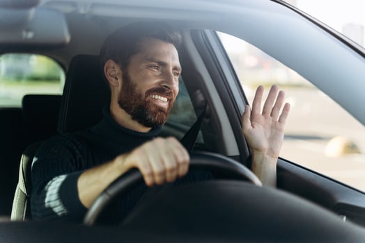 Handsome young smiling driver of car waving hand as a sign of greeting while driving the car with pleasure emotions. Transportation concept photo