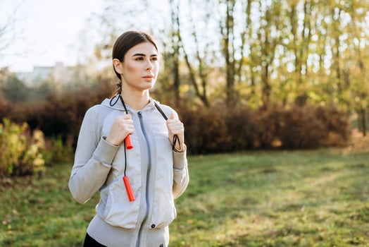 Girl with skipping rope on her shoulders looking thoughtfully, autumn sunny day. photo