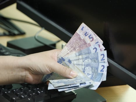 Hand of a woman holding Brazilian money on a computer keyboard photo