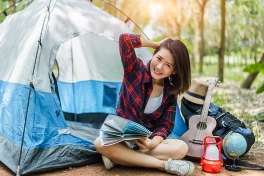 Beautiful Asian woman playing Ukulele in front of camping tent in pine woods. People and Lifestyles concept. Adventure and Travel theme photo