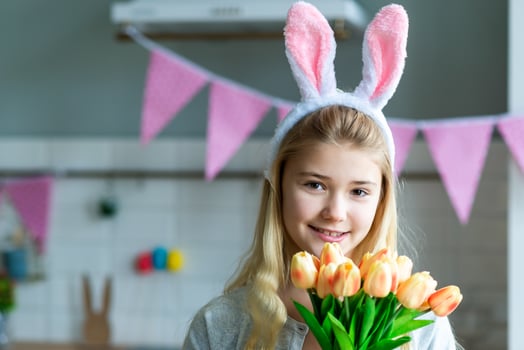 Little girl in holding tulips in white bunnys earrs in hands. Adorable smiling little girl holding flowers. photo