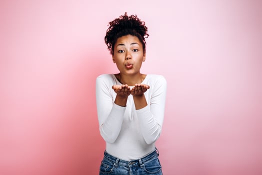 Portrait of a lovely pretty woman sending air kiss while standing and looking at camera isolated over pink background photo