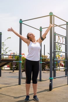 Happy woman working out on the sports ground in sunny summer day, raising arms up, enjoying the sun photo