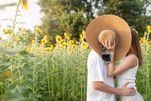 Young happy couple kissing on a picnic blanket, covering their faces with a summer hat photo