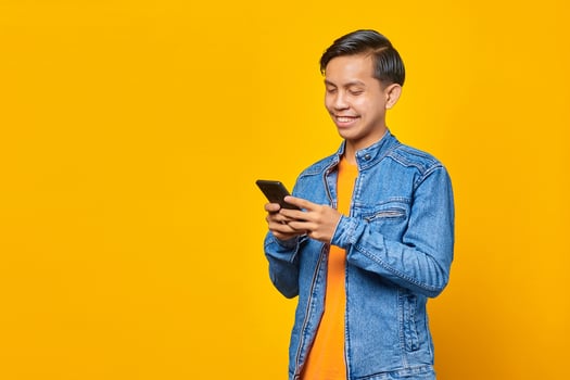Cheerful asian man using smartphone on yellow background photo