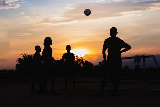 Silhuoette action sport outdoors of a group of kids having fun playing street soccer football for exercise in community rural area . Poor and poverty children in development country photo