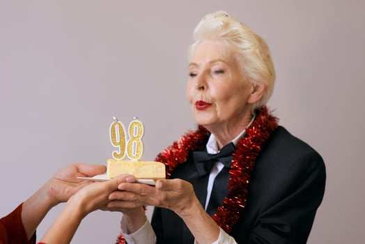 Happy cheerful stylish ninety-eight years old woman in black suit celebrating her birthday with cake. Lifestyle, positive, fashion, style concept photo