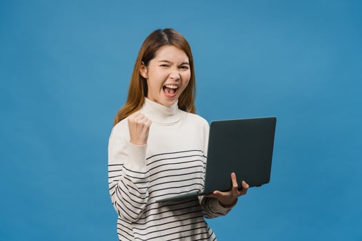 Young Asia lady using laptop with positive expression, smiles broadly, dressed in casual clothing feeling happiness and stand isolated on blue background. Happy adorable glad woman rejoices success. photo