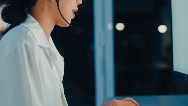 Millennial Asia young call center agent or customer support service executive using computer and microphone headset working technical support in late night office. Telemarketing or sales job concept. photo
