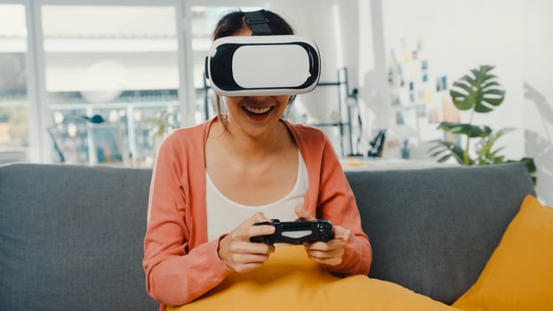 Asian lady wear headset glasses of virtual reality play joystick game on couch in living room at house. Stay at home covid quarantine, Re-imagine reality, VR at home, VR technology of future concept. photo