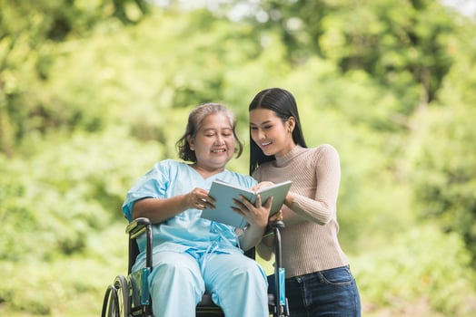 Happy Woman in a wheelchair reading a book with her daughter at the park photo