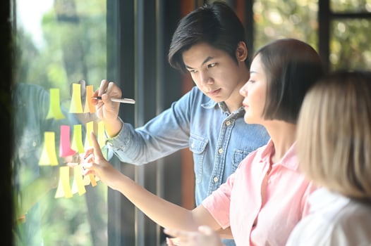 Young men and women at the office are working together. They use a pen and hand to point the note on the glass. photo