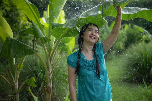 Portrait of a young Asia woman with black hair holding a banana leaf in the raining at the green garden background photo
