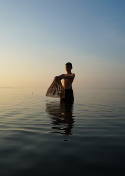 At lake, young asian man using bamboo fish trap to catch fish in the morning photo