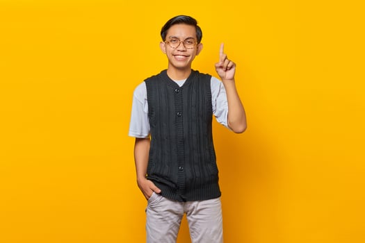 Cheerful asian young man pointing up to copy space isolated over yellow background photo