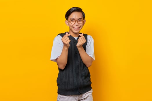 Portrait of smiling young Asian man showing finger hearts over yellow background photo