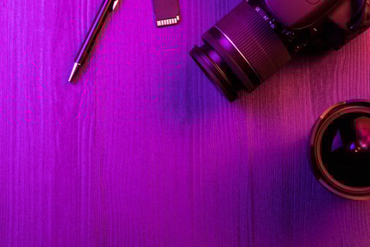 Camera, pencil, fish eye lens and SD card. Pink light. Workspace top view. Copy space. Wood background photo