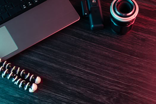 A workspace with laptop, lens and tripod on a wood desk. Freelance or creative man or woman. Red and blue light. Copy space text photo