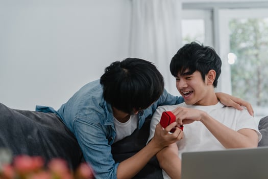 Young Asian gay couple propose at modern home, Teen korean LGBTQ men happy smiling have romantic time while proposing and marriage surprise wear wedding ring in living room at house concept. photo