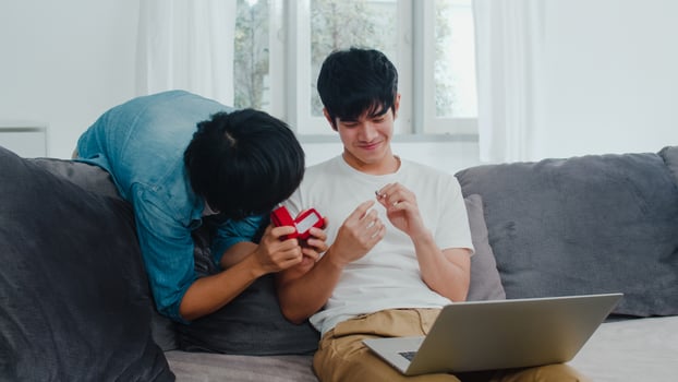 Young Asian gay couple propose at home, Teen korean LGBTQ men happy smiling have romantic time while proposing and marriage surprise wear wedding ring in living room at house concept. photo