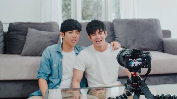 Young Asian gay couple influencer couple vlog at home. Teen korean LGBTQ men happy relax fun using camera record vlog video upload in social media while lying sofa in living room at house concept. photo