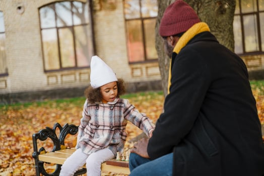 Black grandfather and granddaughter sitting in an autumn park playing chess photo