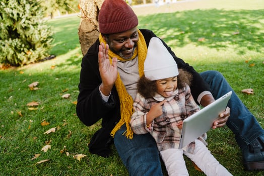 Black grandfather and granddaughter using tablet computer while sitting in a park photo